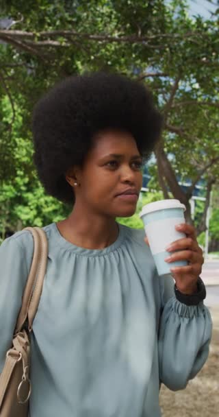 公園でコーヒーを飲みながらアフロ歩くアフリカ系アメリカ人女性の笑顔の垂直ビデオポートレート 身体への包容力や街中で — ストック動画