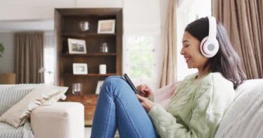 Siyah saçlı, kulaklık ve akıllı telefon kullanan gülümseyen melez kadının videosu. Boş zaman, ev hayatı ve refah yaşam tarzı konsepti.