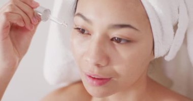 Saçında havlu olan ve banyoya yüz serumu süren gülümseyen melez kadının portresi. Sağlık ve güzellik, boş zaman, ev hayatı ve yaşam tarzı konsepti.