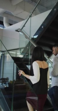 Çift ırklı bir adam ve Asyalı bir kadının bir ofiste merdivenlerden çıkıp tablete baktıkları dikey bir fotoğraf. Şirket çevre kavramı.