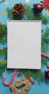 Mavi arka planda Noel süslemeleriyle çevrili bir defterin dikey görüntüsü. Noel konsepti ve telif alanı.