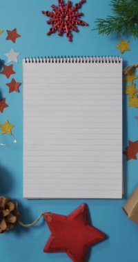 Mavi arka planda Noel süslemeleriyle çevrili bir defterin dikey görüntüsü. Noel konsepti ve telif alanı.