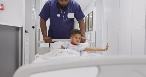 アフリカ系アメリカ人の男性医師が小児患者と一緒に病院のベッドに寝そべって歩く ライフスタイル 病院のコンセプト — ストック動画