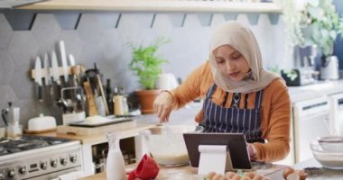 Mutfakta tesettürlü mutlu melez bir kadının tablette tarifini kullanırken videosu. Mutluluk, iletişim, sağlık, kapsayıcılık ve ev hayatı.