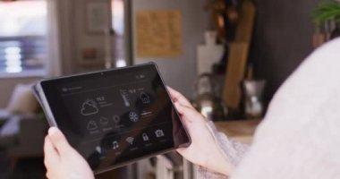 Evde elinde akıllı ev arayüzü ekranlı tablet tutan melez bir kadının orta bölüm videosu. Teknoloji, kontrol, ekoloji ve ev hayatı.