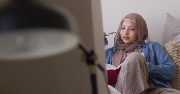 Video Omtänksam Biracial Kvinna Hijab Skriva Anteckningsbok Sitter Vardagsrummet Hemma — Stockvideo
