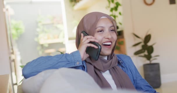 Video Van Glimlachende Biracial Vrouw Hijab Praten Smartphone Ontspannen Woonkamer — Stockvideo