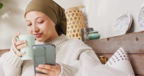 Видео Счастливой Расовой Женщины Хиджабе Пьющей Кофе Пользующейся Смартфоном Дома — стоковое видео