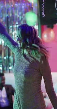 Vertical video of happy caucasian woman dancing on dancefloor at a nightclub. Fun, music, going out and party concept.