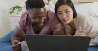 Laptop kullanan ve yatak odasında yatan mutlu çift. Ev kavramında kaliteli zaman geçirmek.