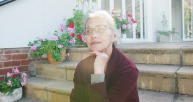 Mutlu Asyalı son sınıf öğrencisi kadın güneşli bir günde bahçede merdivenlerde oturuyor. Etkin emeklilik ve yaşam tarzı kavramı.