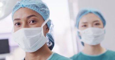 Portrait of smiling biracial female surgeon in cap and face mask in operating theatre, copy space. Hospital, medical and healthcare services.