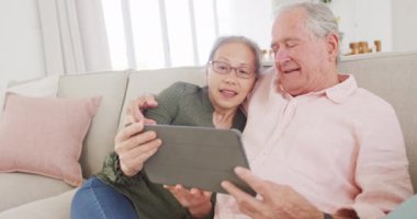 Tablet kullanan ve kanepede oturan mutlu yaşlı çift. Etkin emeklilik ve yaşam tarzı kavramı.