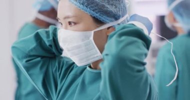 Video of asian female surgeon tying face mask in operating theatre, copy space. Hospital, medical and healthcare services.