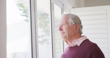 Happy caucasian senior man smiling and looking through window alone. Active retirement and lifestyle concept.