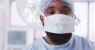 Video portrait of african american male surgeon wearing face mask in operating theatre, copy space. Hospital, medical and healthcare services.