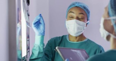 Video of biracial female surgeon discussing x-ray with colleague in operating theatre. Hospital, medical and healthcare services.