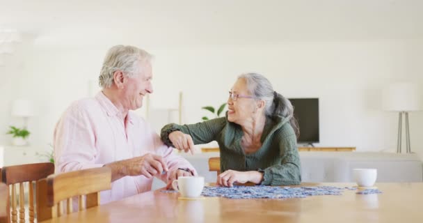 幸せな多様な高齢者のカップルのテーブルに座ってパズルを行う 現役引退とライフスタイルのコンセプト — ストック動画