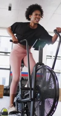 Vertical video of determined african american woman working out at a gym on exercise bike. Exercise, fitness and healthy lifestyle.