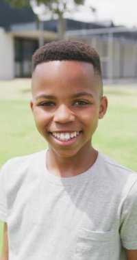 Okul bahçesinde gülümseyen mutlu Afro-Amerikan okul çocuğunun dikey video portresi. Eğitim, çocukluk, kapsayıcılık, okul ve öğrenim kavramı.