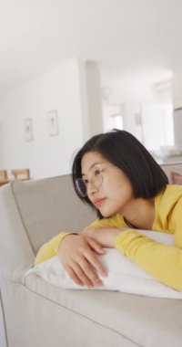 Oturma odasında yatan mutlu Asyalı kadının dikey portresi. Ev kavramında kaliteli zaman geçirmek.