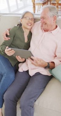 Kanepede oturup tablet kullanan mutlu yaşlı çiftin dikey videosu. Etkin emeklilik ve yaşam tarzı kavramı.
