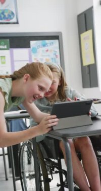 İki mutlu beyaz kız öğrencinin tablet kullandığı dikey video, biri tekerlekli sandalyede, kopyalama alanı. Eğitim, çocukluk, kapsayıcılık, okul ve öğrenim kavramı.