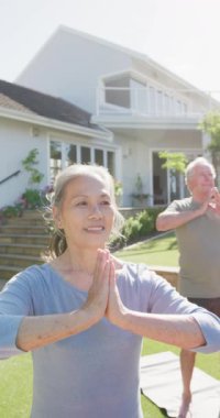 Bahçede yoga yapan mutlu yaşlı çiftin dikey videosu. Etkin emeklilik ve yaşam tarzı kavramı.