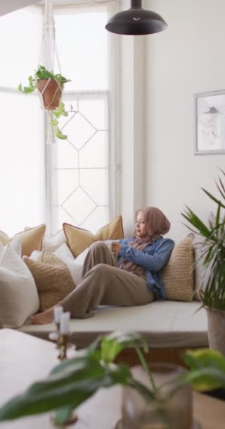 Vertical Video Thoughtful Biracial Woman Hijab Relaxing Sofa Drinking Coffee — Wideo stockowe