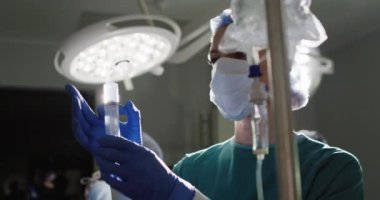 Video of caucasian female surgical assistant preparing drip bag in operating theatre. Hospital, medical and healthcare services.