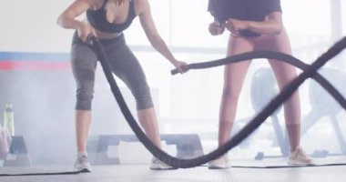Video of diverse female fitness trainer encouraging woman battling ropes working out at a gym. Exercise, fitness and healthy lifestyle.