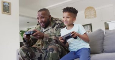 Happy african american father and his son sitting on sofa and playing video games. Spending quality time at home.