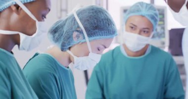 Video of asian female surgeon looking to camera during operation in theatre with diverse colleagues. Hospital, medical and healthcare services.