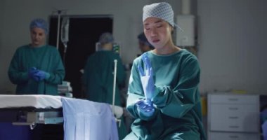 Video of asian female surgeon putting on gloves and looking to camera in opreting theatre. Hospital, medical and healthcare services.