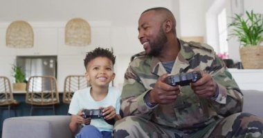 Happy african american father and his son sitting on sofa and playing video games. Spending quality time at home.