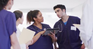 Video of diverse group of male and female doctors looking at tablet talking in hospital corridor. Hospital, medical and healthcare services.