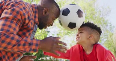 Happy african american father and his son playing football in garden. Spending quality time at home.