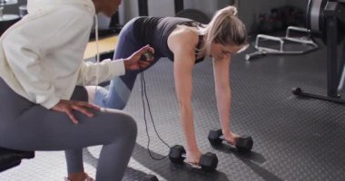 Video of diverse female fitness trainer and determined woman raising dumbbells working out at a gym. Exercise, fitness and healthy lifestyle.