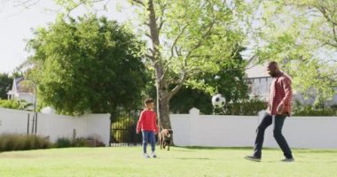 Happy african american father and his son playing football in garden. Spending quality time at home.