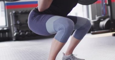 Video of confident, determined caucasian woman squat lifting barbell weights working out at a gym. Exercise, fitness and healthy lifestyle.