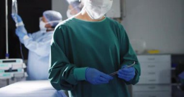 Video of asian female surgeon checking instruments looks to camera in operating theatre, copy space. Hospital, medical and healthcare services.