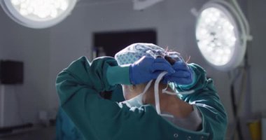 Video of rear view of asian female surgeon tying face mask in operating theatre. Hospital, medical and healthcare services.