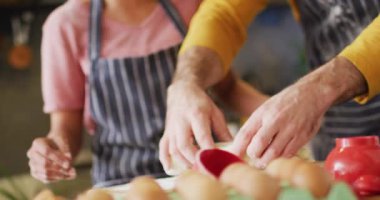 Video of laughing diverse couple in aprons baking together, kneading dough in kitchen. Happiness, inclusivity, free time, togetherness and domestic life.
