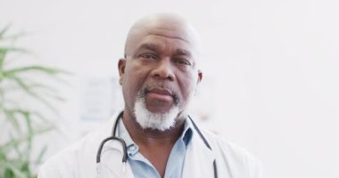 Video portrait of happy senior african american male doctor smiling in hospital corridor. Hospital, medical and healthcare services.