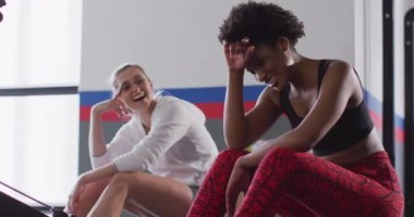 Video of two happy diverse women on rowing machines recovering after working out at a gym. Exercise, fitness and healthy lifestyle.