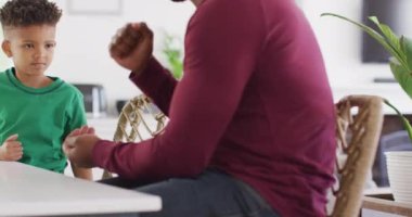 Happy african american man and his son sitting at table and speaking sign language. Spending quality time at home, childhood, deafness and family concept.