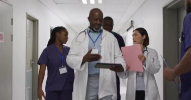 Video of four diverse male and female doctors discussing tablet and files, walking in corridor. Hospital, medical and healthcare services.