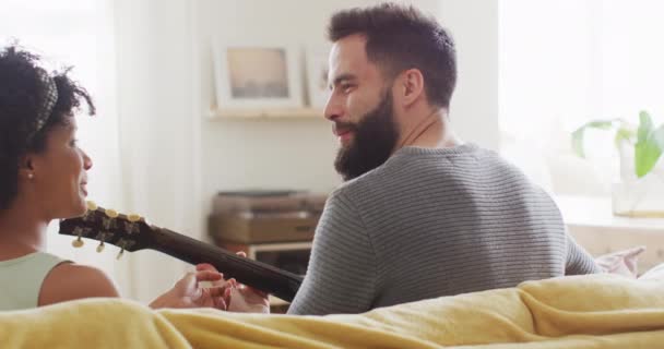 家庭で幸せな多様なカップルのリアビューのビデオでは 男はギターを演奏し 女性に歌い スペースをコピーします 包括性 自由な時間 ロマンス 団結と国内生活 — ストック動画