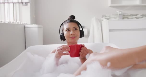 Video Smiling Biracial Woman Headphones Red Cup Tea Bathtub Bubble — Vídeo de stock