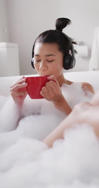 Vertical Video Smiling Biracial Woman Headphones Red Cup Tea Bathtub — Stok video